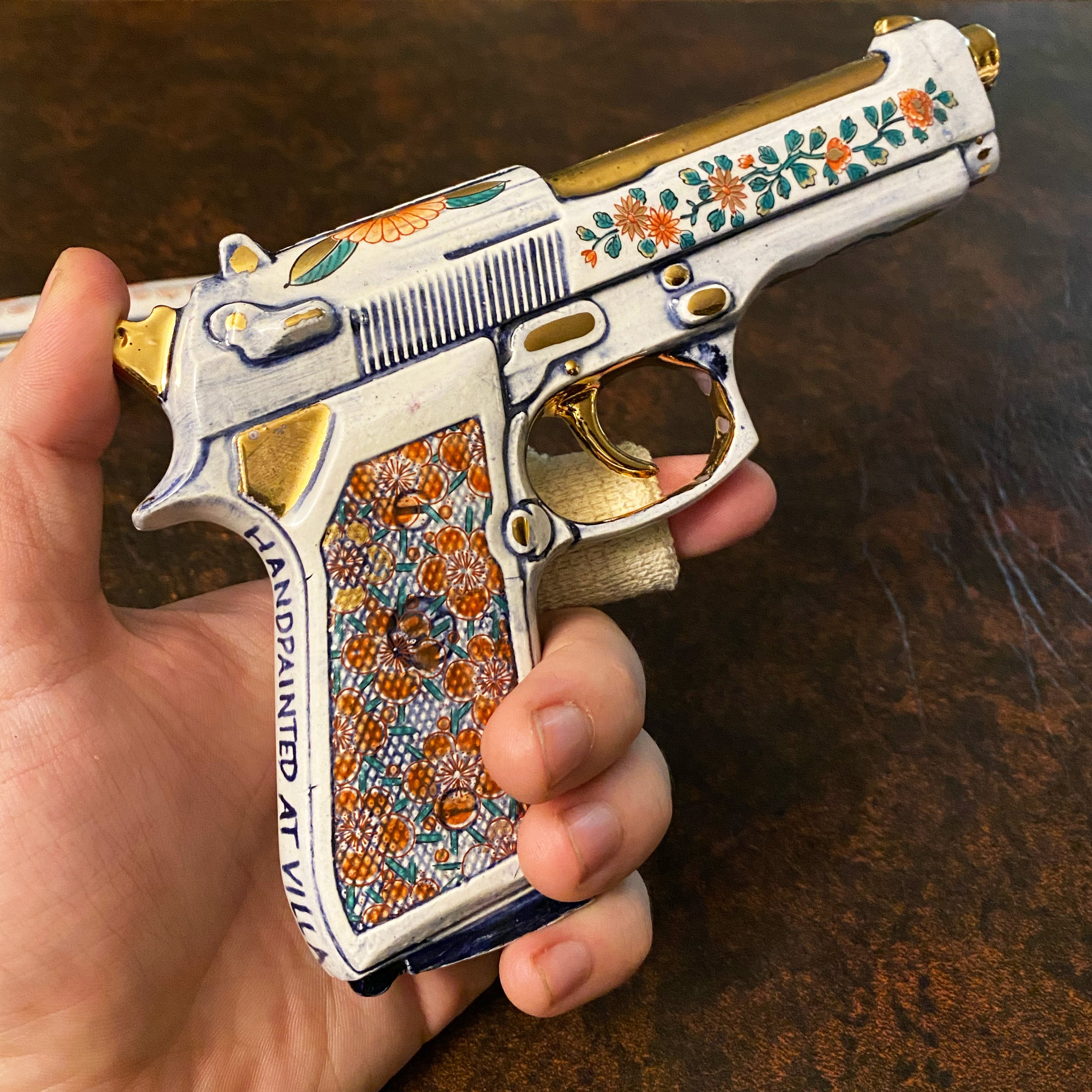 The porcelain Beretta 92 held in hand, showing scale and the hand-painted Imari floral decoration